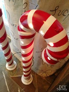 two red and white striped candles are on the floor next to each other in front of a curtain