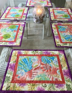 four quilted placemats on a table with a candle in the center and one sitting on a chair