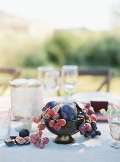 the table is set with grapes and other fruit on it, along with wine glasses