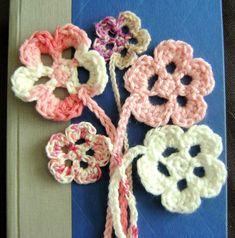 crocheted flowers are placed on top of a blue and white book with pink trim