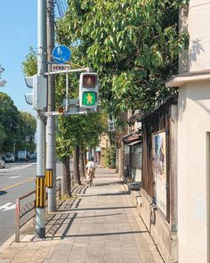 a man walking down the sidewalk next to a traffic light on a city street with trees lining both sides