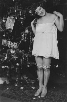 an old photo of a woman in front of a christmas tree with stockings and stockings on