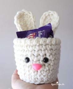 a hand holding a small crocheted bunny cup with candy in it's mouth