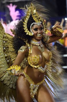 a woman dressed in gold is dancing with feathers on her head and chest, while wearing an elaborate costume