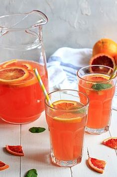 three glasses filled with orange juice and garnished with mint leaves on a white table