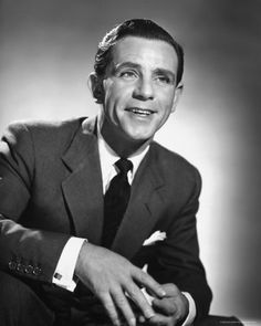 a man in a suit and tie posing for a photo with his hand on the table