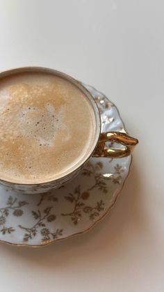 a cup of coffee sitting on top of a saucer next to a plate with gold trim