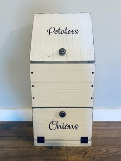 a white wooden box with the words potatoes and onions on it sitting on a wood floor