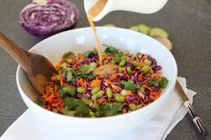 someone pouring dressing into a bowl filled with vegetables