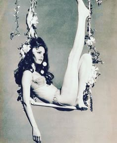 an old photo of a woman on a swing with flowers in her hair and stockings