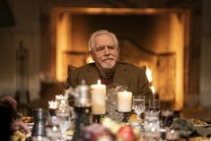 an older man sitting at a dinner table with candles in front of him and food on the side