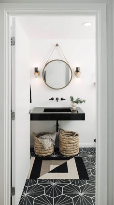 a bathroom with black and white flooring and a round mirror on the wall above it