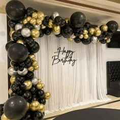 black and gold balloon arch with happy birthday written on the wall in front of it