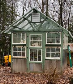 a small green house in the woods surrounded by leaves