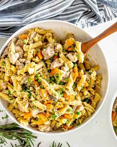 two bowls filled with pasta and vegetables on top of a white tablecloth next to a wooden spoon