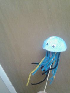 a hand holding a blue and yellow jellyfish on a toothpick with two eyes