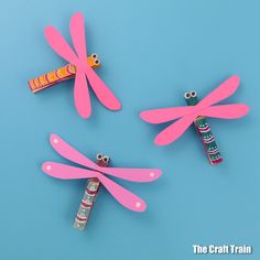 three pink dragonflys made out of construction paper and candy sticks on a blue background