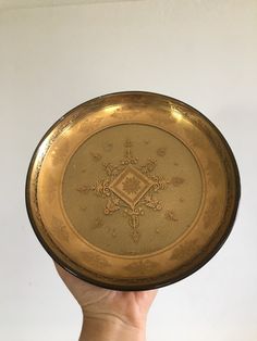 a hand holding a gold plate with an ornate design