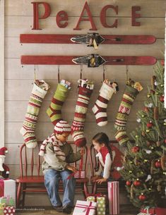 two young boys sitting on a bench with christmas stockings hanging from the wall behind them