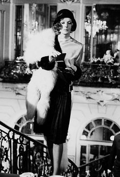 a woman in a dress and fur stoler standing on the steps of a building