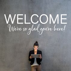 a woman standing in front of a wall with the words welcome, we're so glad you're here