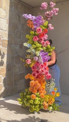 a woman standing next to a tall vase filled with colorful flowers on top of a sidewalk