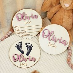 three personalized wooden discs with baby's feet and name on them next to a teddy bear