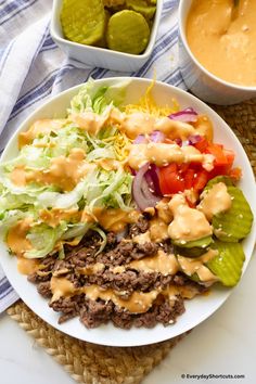 a white plate topped with lettuce, meat and dressing next to two bowls of dip