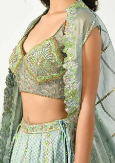 Go classy yet modern with this beautiful piece of attire. The grey-blue hued pleated lehenga has geometric and floral prints highlighted with hand and machine embroidery, the corset style blouse has multi colored sequins and beads to define the motifs, bringing an ethereal look. The key highlight, the cape has the cutwork at the border and pleats at one side making it look like a draped dupatta. Machine Embroidery Lehenga, Fitted Multicolor Embellished Sets, Fitted Embellished Multicolor Sets, Fitted Hand Embellished Dupatta For Navratri, Hand Embellished Fitted Dupatta For Navratri, Fitted Embellished Multicolor Sharara, Fitted Multicolor Embellished Sharara, Designer Choli With Intricate Embroidery For Festive Occasions, Designer Embroidered Choli For Reception