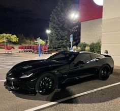 a black sports car parked in front of a gas station at night with its lights on