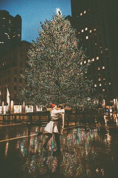 a man and woman dancing in front of a large christmas tree on a city street