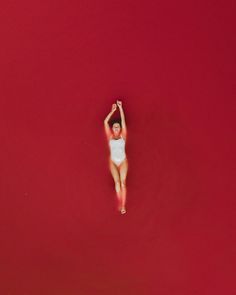 an aerial view of a woman in a white bodysuit floating on red water with her arms up