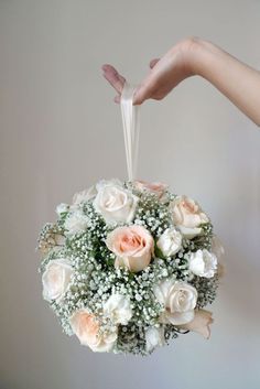 a person holding a bouquet of white and pink roses with baby's breath in it