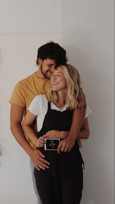 a man and woman embracing each other in front of a white wall