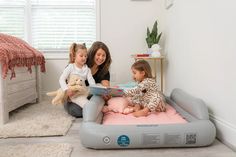 a woman and two children are sitting on an inflatable bed with a book