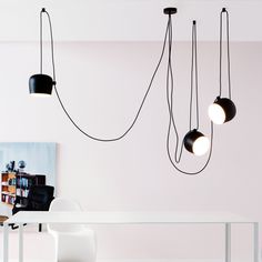 three black and white lights hanging from the ceiling above a table with chairs in front of it