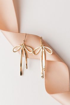 "🎀\"BOW\"🎀 them all away with the perfect set of dainty gold ribbons! Our Gold Ribbon Earrings feature a 14k gold filled hook and 14k gold filled ribbon.  Earrings measure approx. 1.8\" x .6\" Thank you so much for shopping with GGC! By supporting a small business, you are supporting a dream, a family, and so much more! We are so grateful for you! We hope to create with you again soon! ✨LOOKING FOR MORE EARRINGS?✨ Check out our other listings here: https://www.etsy.com/shop/GoldenGratitudeCol?ref=simple-shop-header-name&listing_id=1157209858§ion_id=37356619" Earrings Flatlay, Infinite Jewelry, Jewelry Mood Board, Valentines Day Earrings, Thanksgiving Jewelry, Ribbon Earrings, Photo Concept, Earrings Aesthetic, Simple Hair