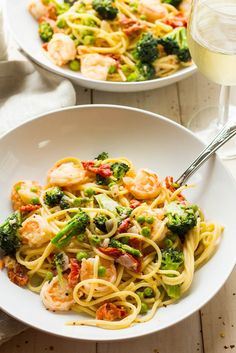 two bowls of pasta with shrimp and broccoli on the side, next to a glass of wine