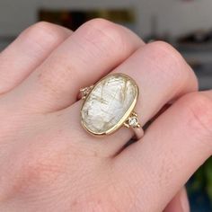 a woman's hand holding a ring with a large stone in the middle and diamond accents on it