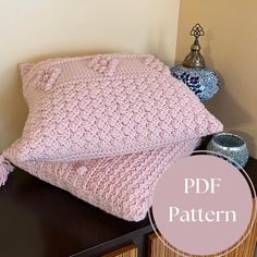 two pink knitted pillows sitting on top of a wooden table next to a vase