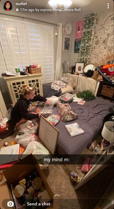 a woman sitting on top of a bed in a room filled with boxes and other items