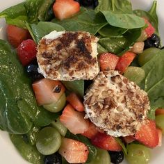 a salad with spinach leaves, strawberries and cheese on top is served in a white bowl