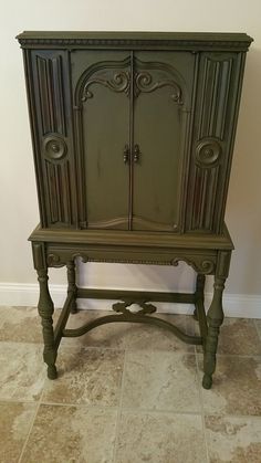 an old fashioned green cabinet sitting on top of a tile floor next to a wall