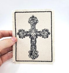 a hand holding up a small cross on top of a white surface with black trimmings