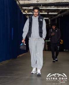 a man in grey sweatpants and black vest walking down a hallway with other people