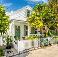 a bicycle parked in front of a white house with green shutters and palm trees