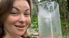 a woman is holding up a water pitcher in front of her face and smiling at the camera