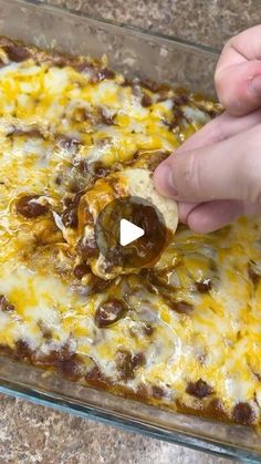 a person dipping some food into a casserole dish with cheese and olives