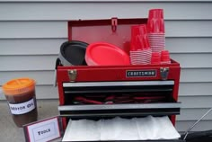 a red toolbox with plates and cups in it sitting next to a cup holder