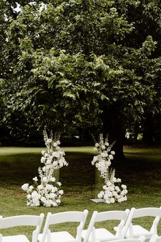 two white chairs are set up in the grass for an outdoor ceremony with flowers and greenery